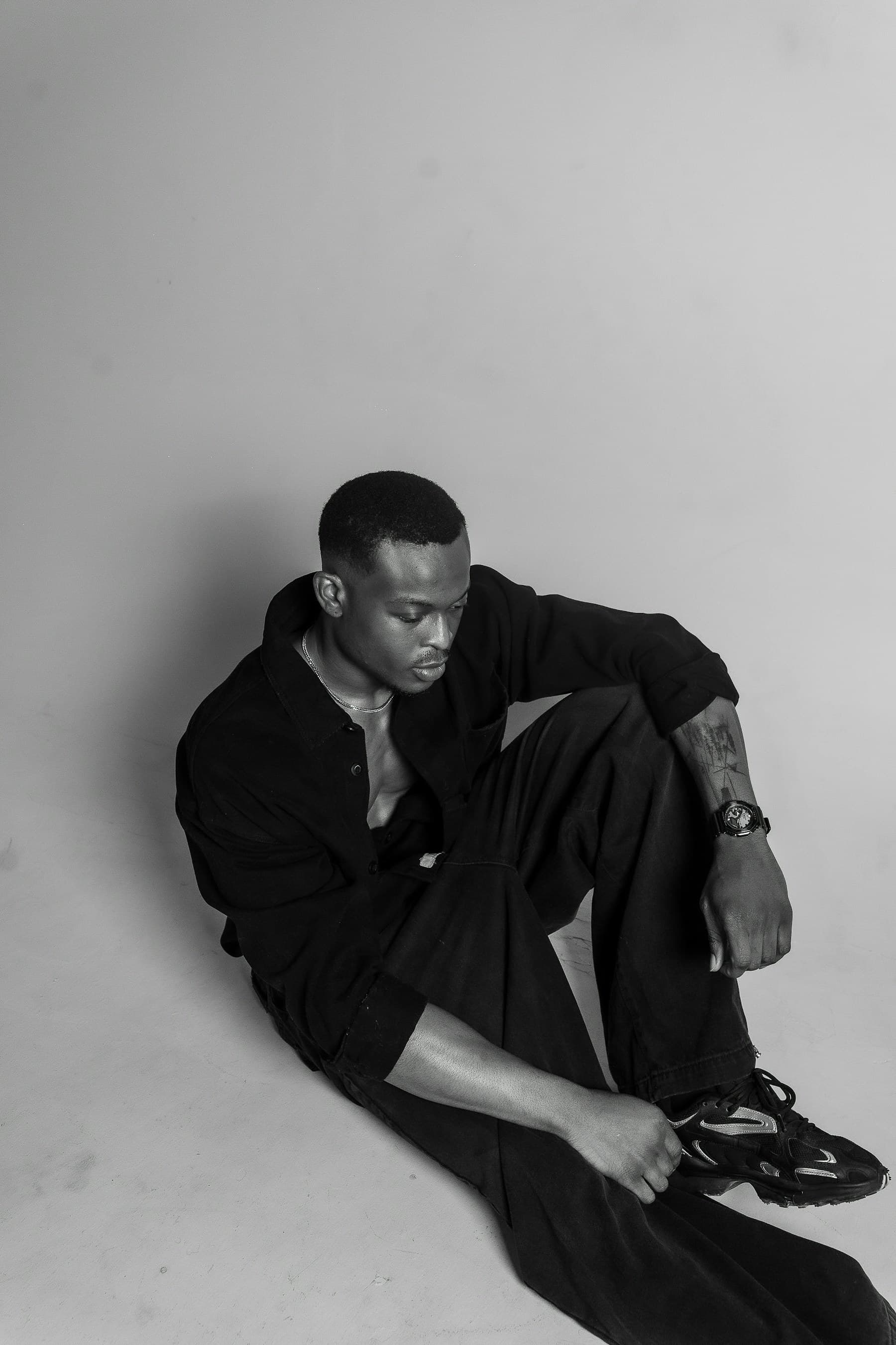 Seated model wearing relaxed black clothing in a light studio